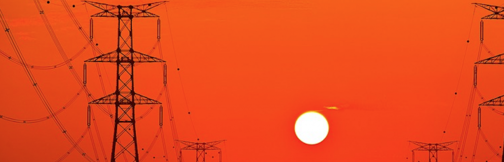 Stromoberleitung vor einem Sonnenball, der den Himmel orange verfärbt.