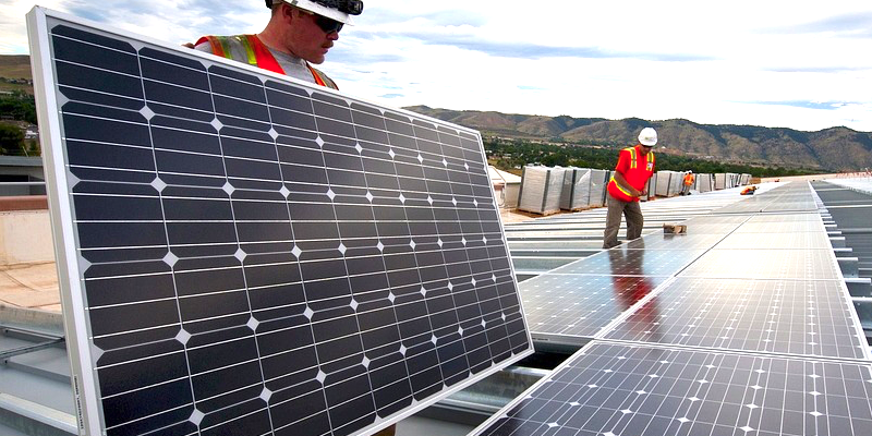Arbeiter bauen eine Photovoltaikanlage auf. Im Hintergrund sind Berge zu sehen.