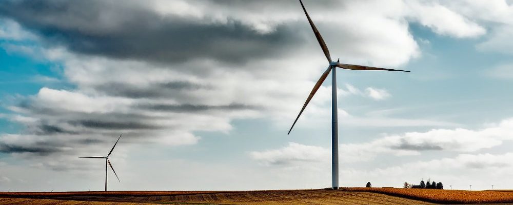 Windkraftanlage auf einem Feld Eine Windkraftanlage im Vordergrund und eine weitere im Hintergrund stehen auf einem abgeernteten Getreidefeld. Der Himmel ist mit grauen Wolken bedeckt.