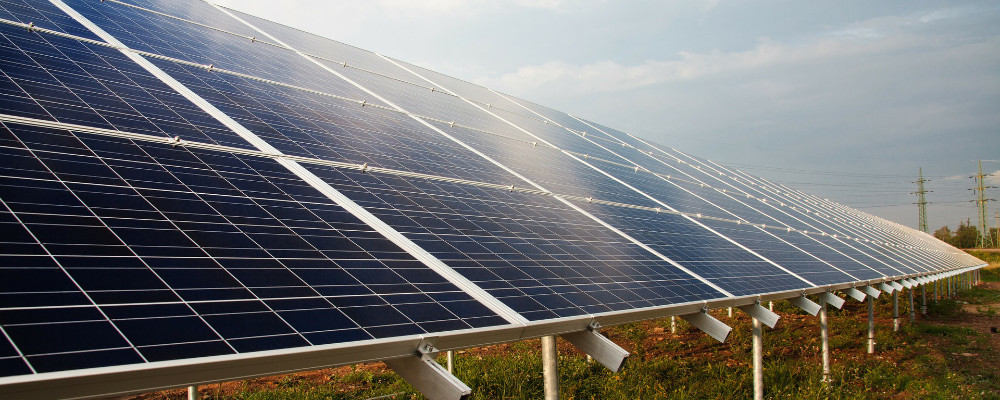 Photovoltaikanlage Eine schräge Fläche mit Solaranlagen steht auf einer Wiese. Im Hintergrund sind Stromanlagen.