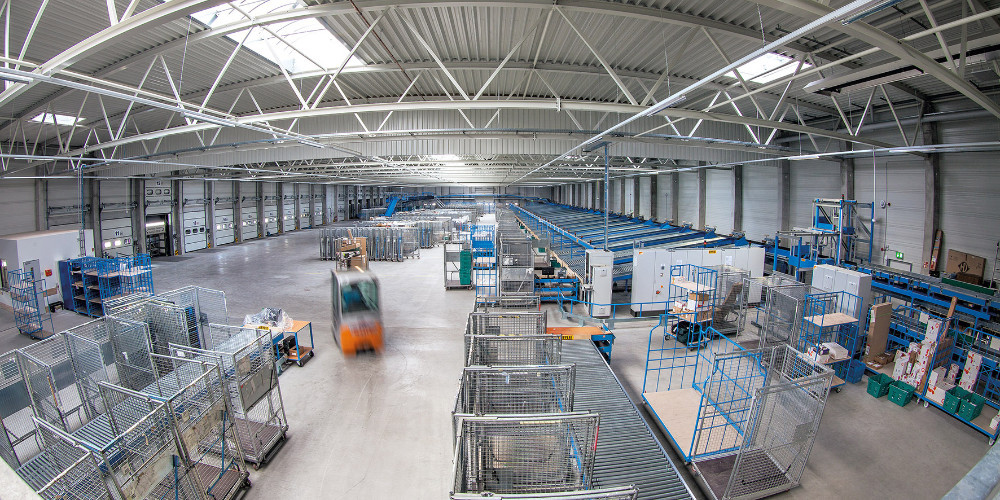 Große Logistikhalle von innen mit verschieden Logistikstationen. Mittig fährt ein Gabelstapler.