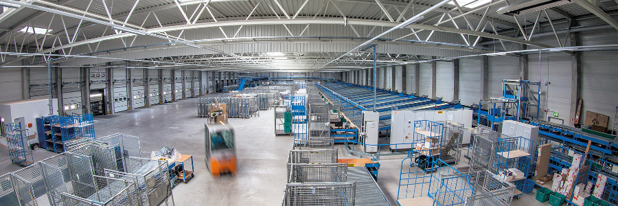 RealEstate_Oranienburg_2695_Web-Beitrag Große Logistikhalle von innen mit verschieden Logistikstationen. Mittig fährt ein Gabelstapler.